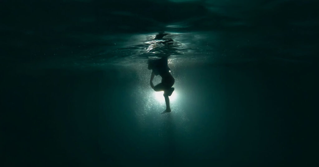 Person submerged in dark water with light below representing salvation and grace