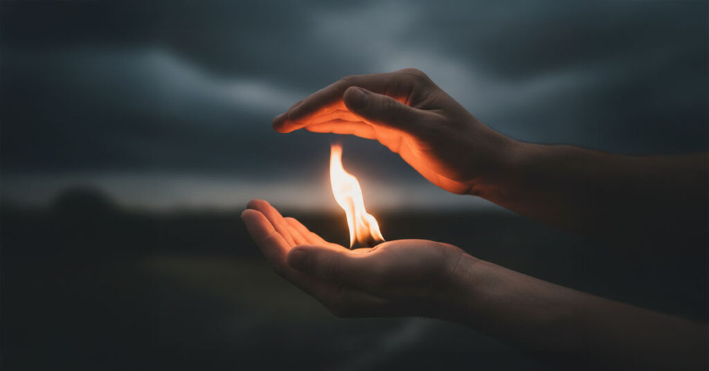A single candle flame burning in darkness representing the fire of love overcoming hatred and bitterness